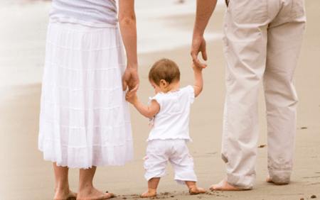 parents holding hands with baby at beach