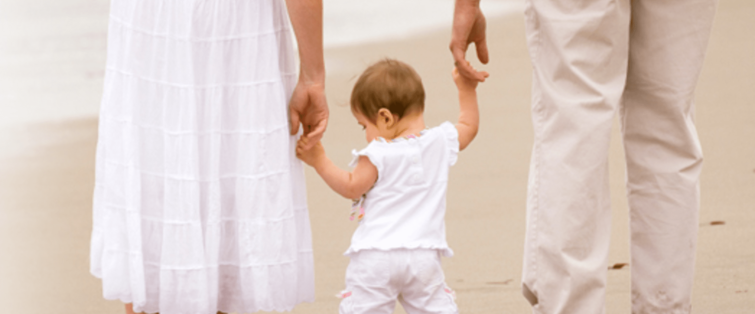 parents holding hands with baby at beach