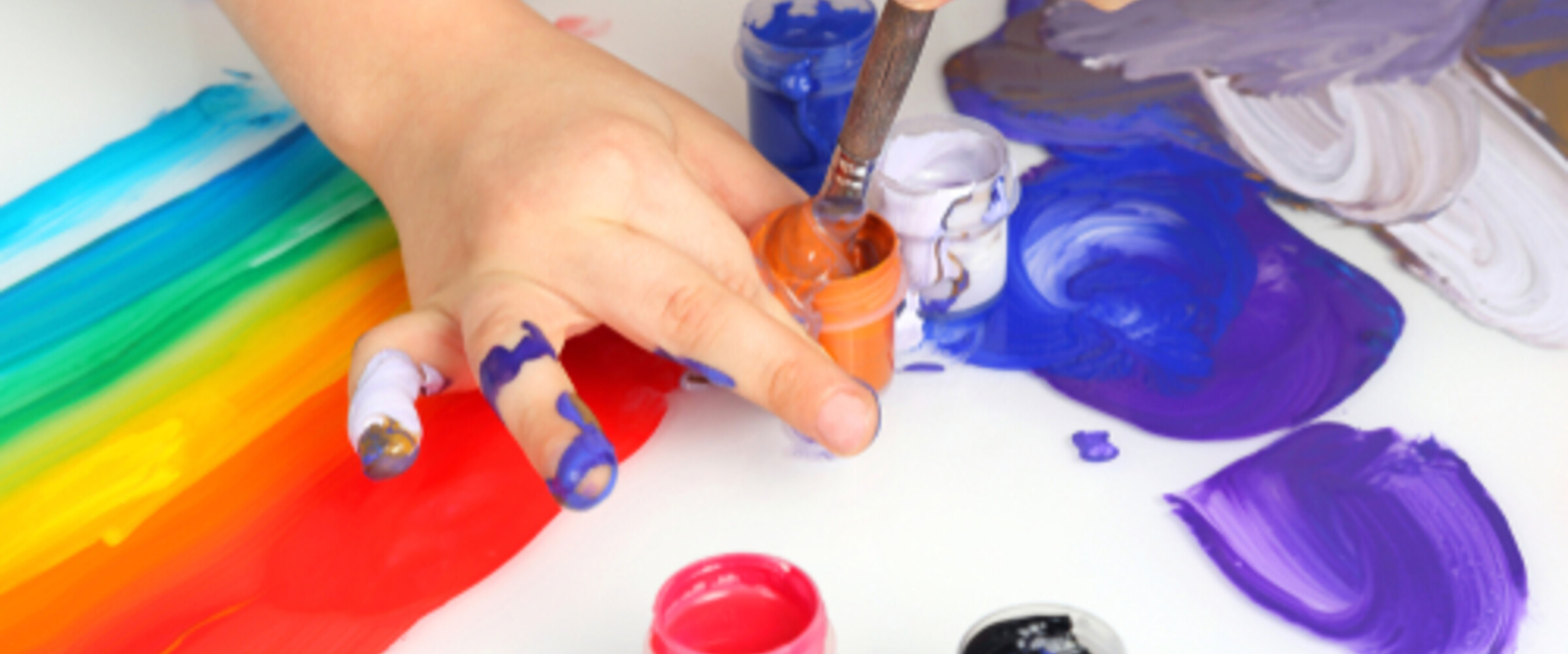 child's hands doing a messy rainbow painting